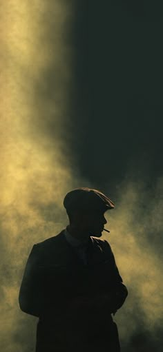 a silhouette of a man wearing a suit and hat with clouds in the sky behind him