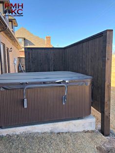 an outdoor hot tub in front of a house with a wooden fence and brown siding