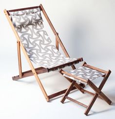 a folding chair with a pillow on it sitting in front of a white wall next to a wooden stand