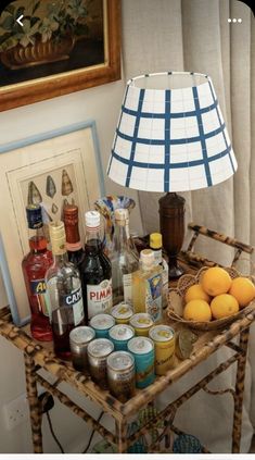 a table that has some bottles and oranges on it with a lamp next to it