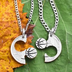 two silver necklaces with basketball charms hanging from it's sides on a leaf