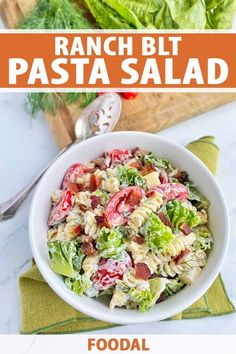 a bowl filled with pasta salad on top of a wooden cutting board next to lettuce