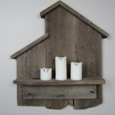 two white candles sitting on top of a wooden shelf next to a house shaped candle holder