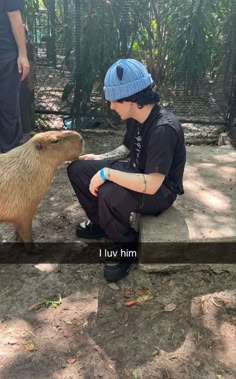 a man sitting on top of a wooden bench next to a capy animal