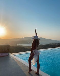 a woman standing on the edge of a swimming pool with her arms in the air