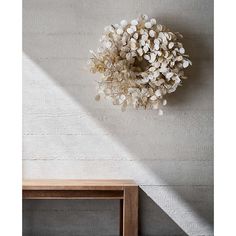 a white wreath hanging on the wall next to a wooden chair and table in front of it