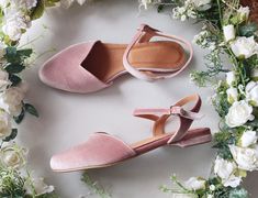 two pairs of pink shoes sitting on top of a white table next to some flowers