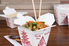 there are four takeout boxes with chopsticks in them and some food on the table