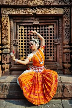 a woman in an orange and white dress dancing on the steps with her hands up