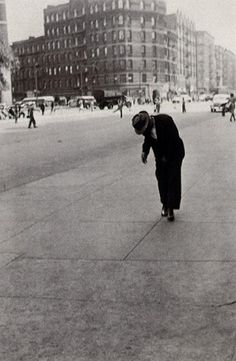 an old black and white photo of a man bending over to pick up something from the ground