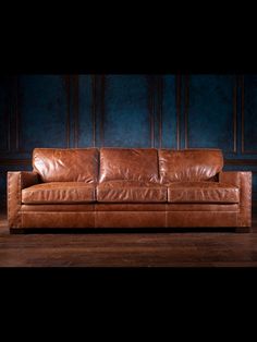 a brown leather couch sitting on top of a wooden floor next to a blue wall