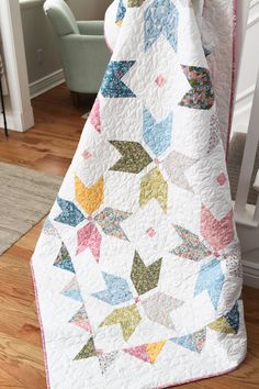 a white quilt with multicolored stars on it sitting on top of a wooden floor