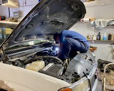 a man working on the hood of a car in a garage with other cars and tools