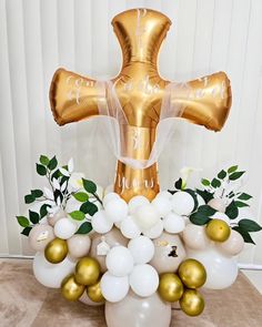 a balloon bouquet with white and gold balloons in the shape of a cross, surrounded by greenery