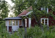 a small red and white house in the woods with lots of flowers around it's windows