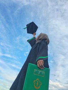 a person wearing a graduation gown and holding a green book in front of the sky