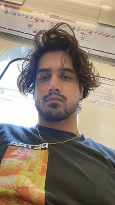 a man with long hair sitting on a bus looking off to the side while wearing a tshirt