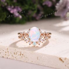 a white opal and diamond ring sitting on top of a stone