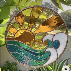 a stained glass sun catcher hanging from a tree in front of some plants and water