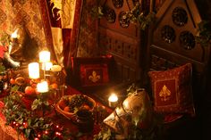 a table with candles and decorations on it in a room filled with red curtains, wall hangings and other items