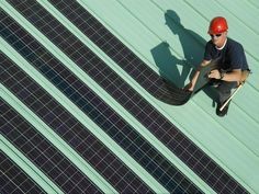 a man sitting on top of a roof next to a solar panel covered in black tiles