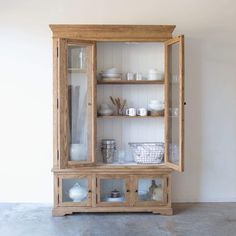 a wooden china cabinet with glass doors and dishes on the top shelf, in front of a white wall