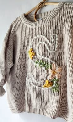 a sweater with flowers is hanging on a clothes hanger and has the word love written in it