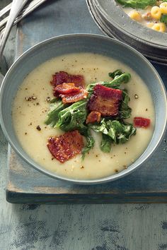 two bowls of soup with bacon, corn and spinach on a tray next to silverware