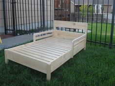 a wooden bed sitting in the grass next to a black iron fence and some green grass