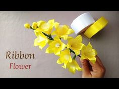 a hand holding yellow flowers next to a roll of ribbon