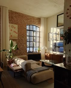 a living room filled with furniture next to a brick wall and large windows in the background