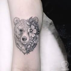 a black and white photo of a bear's head with flowers on its arm