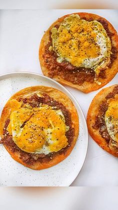 three small pizzas with an egg on top are sitting on a white plate next to each other