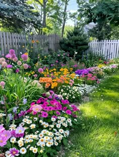 a garden filled with lots of flowers next to a white picket fence and green grass