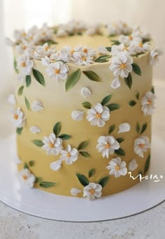 a yellow and white cake with flowers on the frosting is sitting on a plate