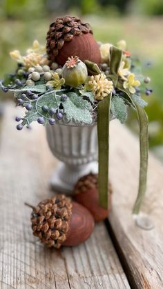 a vase filled with flowers and pine cones on top of a wooden table next to an acorn