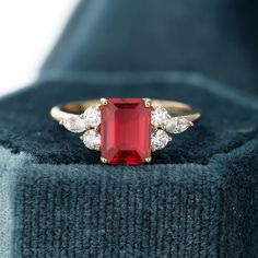 a red stone ring sitting on top of a blue velvet box with two diamonds around it