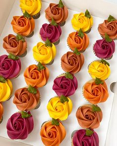 cupcakes decorated with multicolored icing in a white box on a table