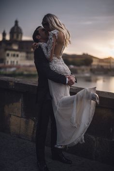 black and white photo of a couple kissing on the bridge in front of a body of water