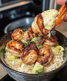 someone is dipping sauce on shrimp over rice in a bowl