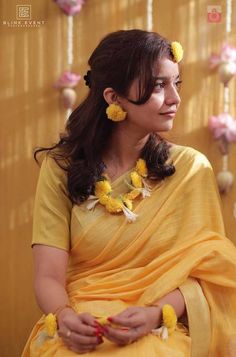 a woman sitting down in a yellow sari with flowers on her head and hands