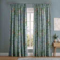 a living room with blue walls and floral curtains on the window sill, along with a rug