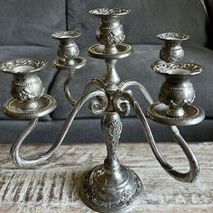 an ornate silver candelabra with five candles on it, in front of a couch