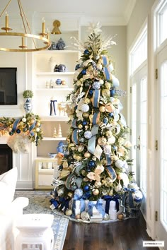 a decorated christmas tree with blue and gold ornaments in a living room area next to a fireplace