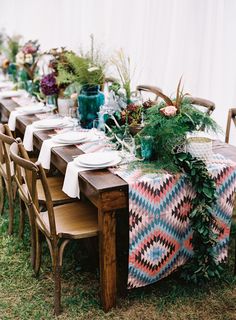 a table set up with flowers and greenery for a wedding or reception in the grass