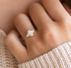 a woman's hand with a diamond ring on top of her finger, wearing a white sweater