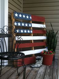 an american flag made out of wood sitting on top of a wooden deck next to potted plants