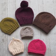 six knitted hats laid out on a white wooden surface with one hat in the middle