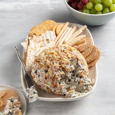 cheese and crackers on a plate next to a bowl of grapes