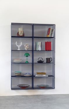 a metal shelf with books and other items on it in an empty room next to a white wall